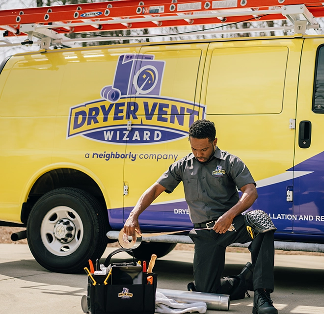 Technician kneeling with toolbox near branded Dryer Vent Wizard van.