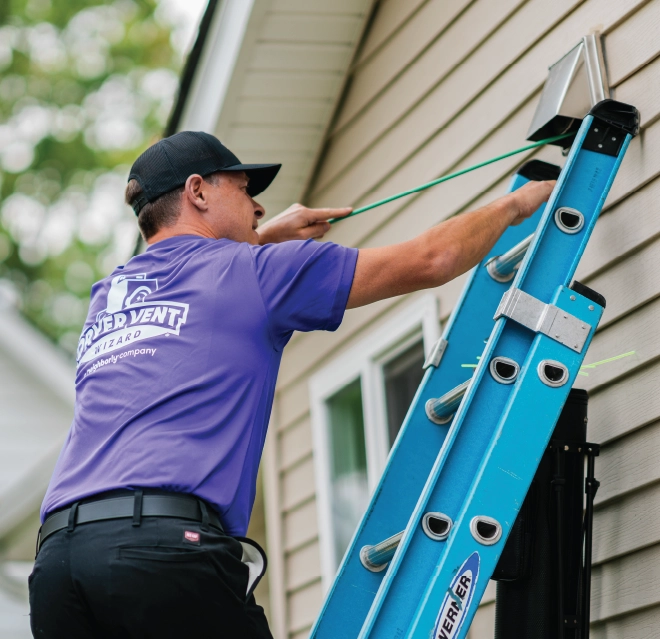 Dryer vent cleaning pro standing on ladder outside home cleaning dryer vent line.