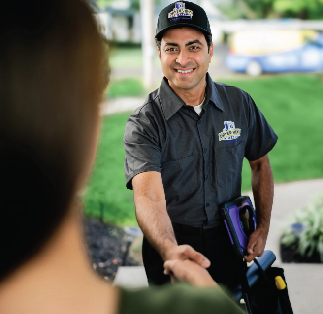 A homeowner greets a Dryer Vent Wizard pro at the front door and shakes hands.