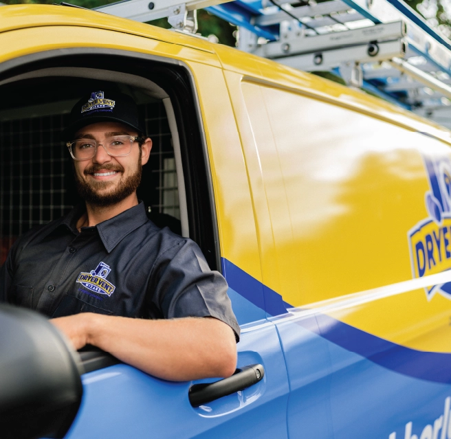 A residential dryer vent pro sits in the front seat of a Dryer Vent Wizard company van smiling.