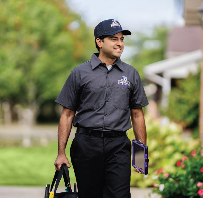 A smiling professional in uniform walks up to home with toolbag.