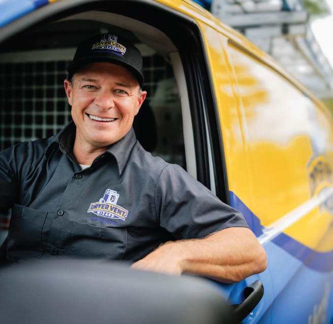 A smiling Dryer Vent Wizard professional sits in the front seat of the company van.