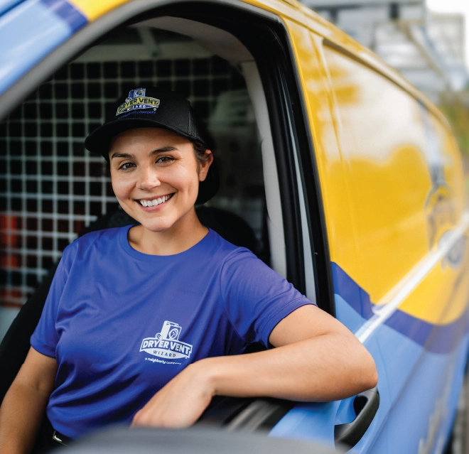 Friendly female dryer vent cleaner smiles from front seat of Dryer Vent Wizard company van.