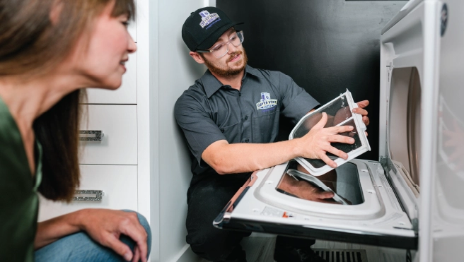 Homeowner and dryer vent cleaning pro kneel and inspect dryer vent screen during inspection.