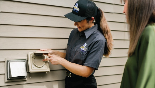 A dryer vent cleaning pro tightens a bolt on a residential dryer.