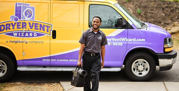 Smiling technician walking with tool bag in front of branded work vehicle.