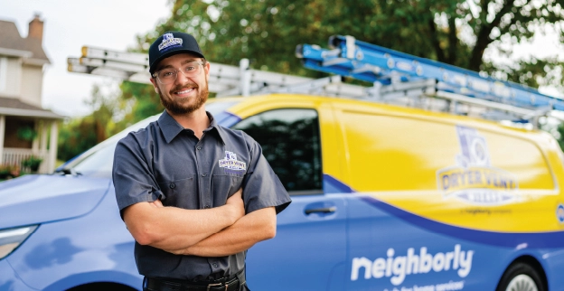 A male, uniformed Dryer Vent Wizard professional stands in front of company van smiling.