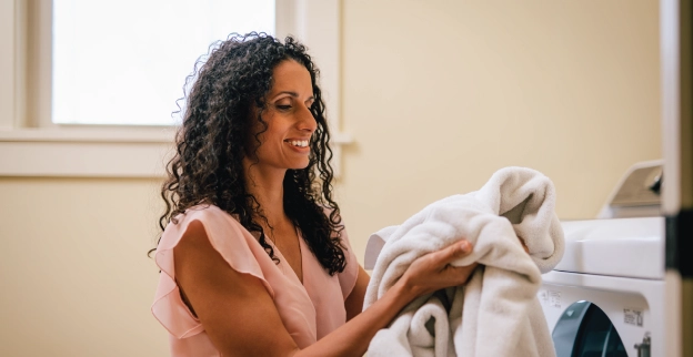 A woman smiles in satisfaction as she removes clean blankets from her dryer