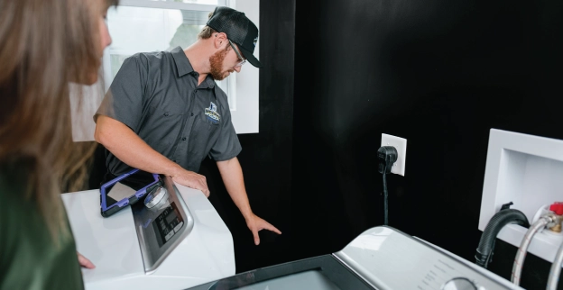 A dryer vent cleaning pro inspects residential dryer vent line while homeowner watches.