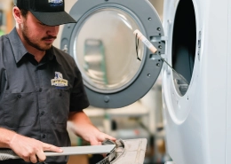 Dryer vent cleaning professional from Dryer Vent Wizard inspecting commercial dryers and looking at clipboard.