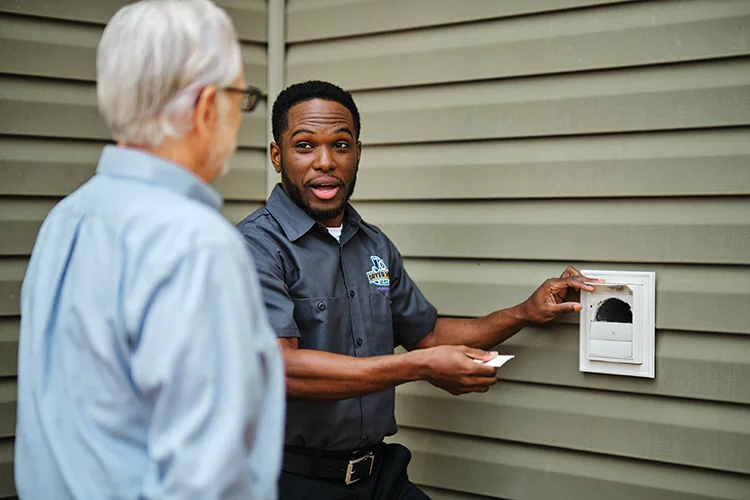 Dryer Vent Wizard technician outside explaining vent debris & clog removal services to a customer