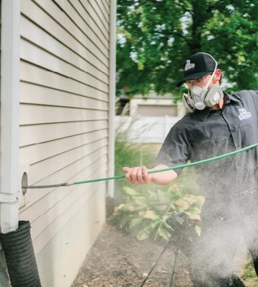 A dryer vent cleaner from Dryer Vent Wizard stands outside of a home cleaning a duct vent line.