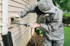 Dryer Vent Wizard professional outside of home in protective gear and mask cleaning dryer vent duct.