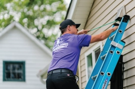 Dryer vent cleaning professional standing on ladder outside of home cleaning dryer duct.