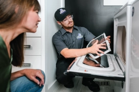 Male dryer vent cleaning professional holding lint trap and speaking with female homeowner.