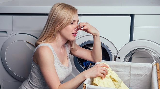 Blonde female next to washing machine dirty laundry basket.