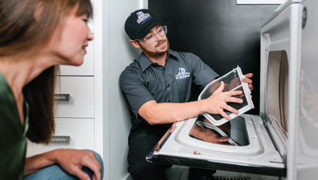 Male dryer vent cleaning professional holding lint trap and speaking with female homeowner.