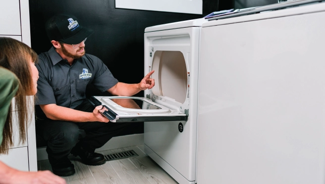 Male Dryer Vent Wizard professional pointing to inside of dryer while speaking with female homeowner.