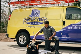 Dryer Vent Wizard tech kneeling with tools in front of branded service vehicle.