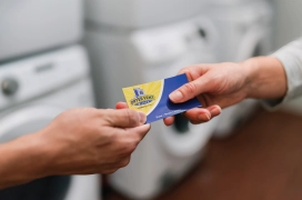 Two individuals both holding one end of a Dryer Vent Wizard business card.