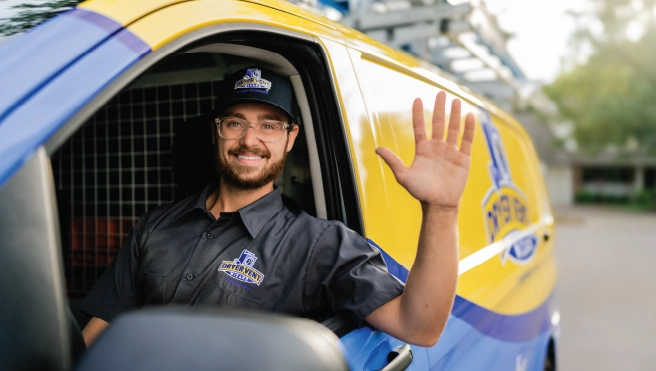 Uniformed Dryer Vent Wizard professional in driver seat of company van smiling and waving.