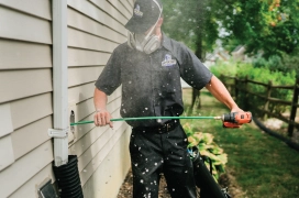 Dryer vent cleaning professional wearing face mask cleans a residential dryer vent from the exterior of a home.