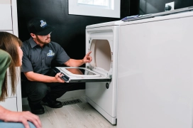 A woman and a professional dryer vent cleaning professional look inside her dryer in laundry room.