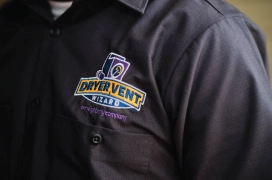 Up close view of a black professional shirt with the yellow, white and purple Dryer Vent Wizard logo.