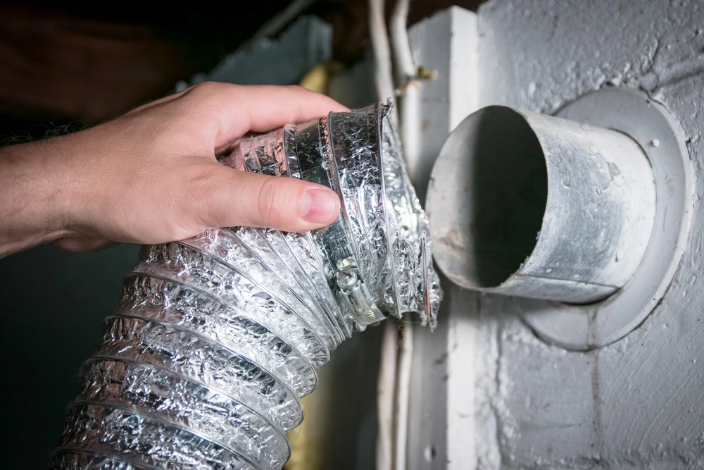 Persons hand holding dryer vent that is not connected.