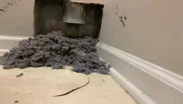 A pile of dryer lint sitting below a dryer vent.