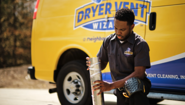 Technician kneeling in front of Dryer Vent Wizard van.